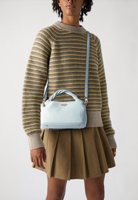Borsa strutturata azzurro chiaro con manico superiore e tracolla removibile. Pelle texture, hardware in argento e quattro piedini metallici alla base.