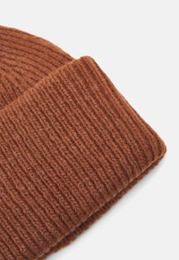 Brown knitted beanie featuring a ribbed texture. The fabric appears thick and warm, with a folded cuff detail for a snug fit.