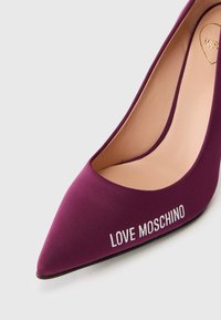 Vijolična visoka pete s koničastim prstom z gladko teksturo in belim napisom "LOVE MOSCHINO" na strani.