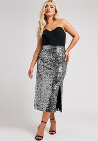 Svart bandeau-top som kombineras med en midi-kjol i silverpaljetter med en sidöppning. Outfiten har en figurnära silhuett och en glänsande textur.