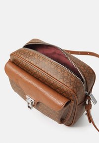 Borsa a mano in pelle marrone con design testurizzato, minuteria in argento e fodera bordeaux. Presenta una chiusura con zip e un ulteriore gancio frontale.