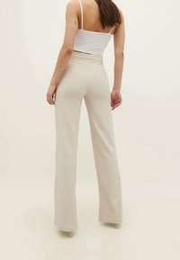 Cream-colored, high-waisted pants with a straight leg design, made of ribbed fabric, featuring an elastic waistband for comfort.