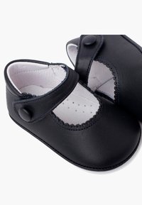 Scarpe Mary Jane in pelle nera con punta arrotondata, bordi scallop e una fibbia con bottone. L'interno ha una morbida fodera bianca con perforazioni.