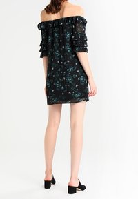 Off-the-shoulder black dress with layered ruffle sleeves and floral pattern in green and purple. Made of lightweight fabric, knee-length.