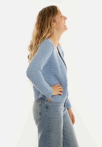 Lichtblauwe gebreide cardigan met een textuurpatroon, open voorkant en lange mouwen, gecombineerd met hooggeprijsde lichte denim jeans.
