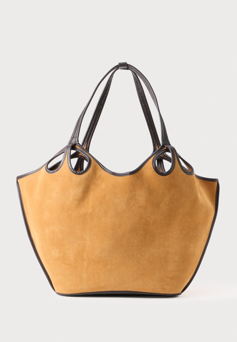 Suede tote bag in mustard with black leather trim. Features dual handles and a rounded shape. Soft texture, minimalistic design.
