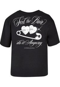 Zwart t-shirt met een grafische print op de achterkant met witte cursieve tekst en twee gestileerde harten die verbonden zijn door een veiligheidsspeld.