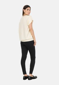 Cream, soft fabric top with drop shoulders, paired with black skinny jeans and black shoes. The top has a relaxed fit and rounded hem.