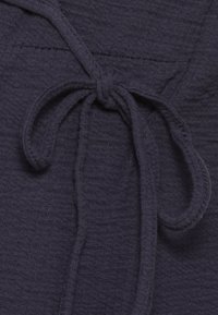 Närbild av ett mörkt texturerat tyg med en knuten rosett gjord av ett matchande tygband.