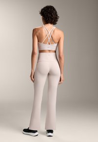 Ljusbeige sportbh med korsade axelband, kombinerad med högmidjade beige tights som vidgar sig längst ner, kompletterad med svarta sneakers.