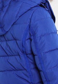 Chaqueta tipo puffer azul con capucha, que presenta un diseño acolchado y una textura suave, destacada por detalles de patrón tonal y costuras en contraste.