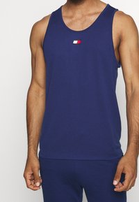 Canotta senza maniche blu navy realizzata in tessuto morbido, con un piccolo logo in rosso, bianco e nero sul petto. Design aderente.