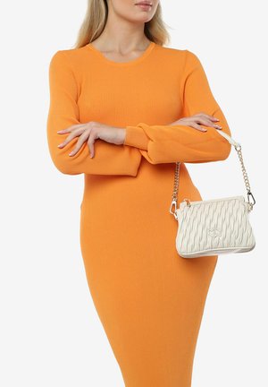Witte gewatteerde handtas met een kettingstrap, met een getextureerd golfpatroon. Model draagt een oranje geribbelde jurk.