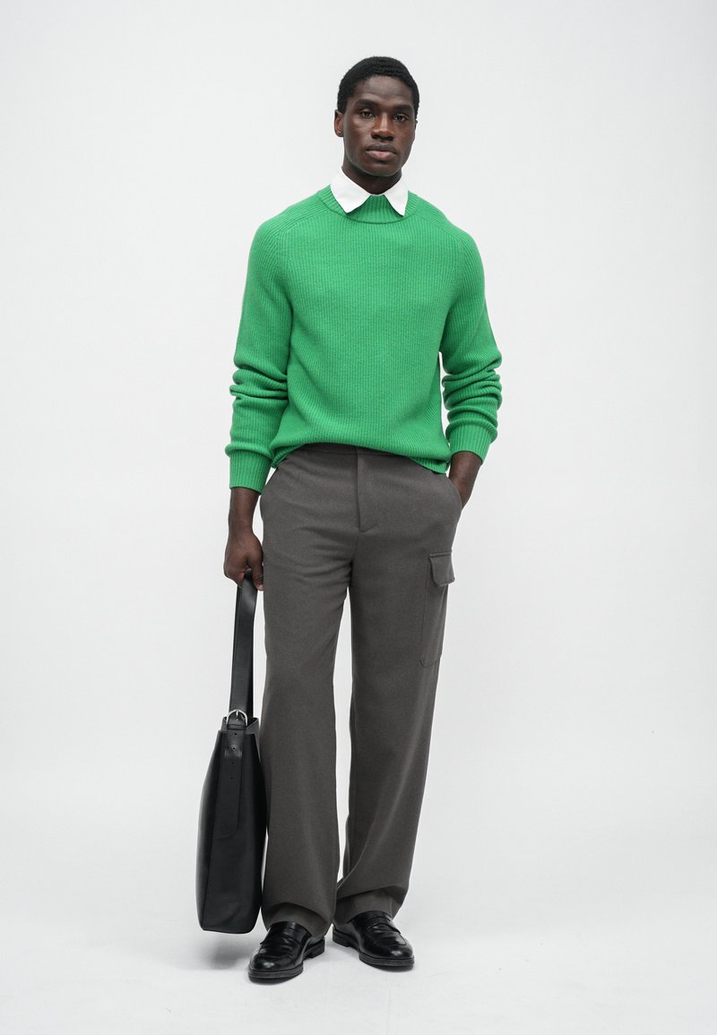 Pull vert à côtes, chemise blanche à col, pantalon gris à large jambe, sac en cuir noir et chaussures noires. Design simple, tissu texturé.