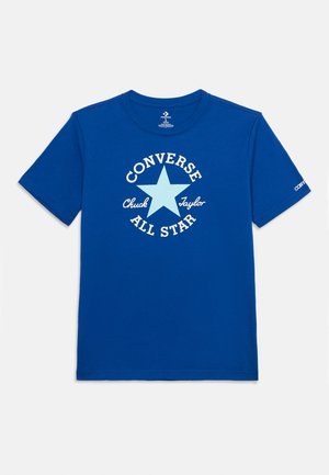Tricou albastru cu mâneci scurte, cu o stea albastru deschis și text alb „Converse Chuck Taylor All Star” pe față și „Converse” pe mâneca stângă.