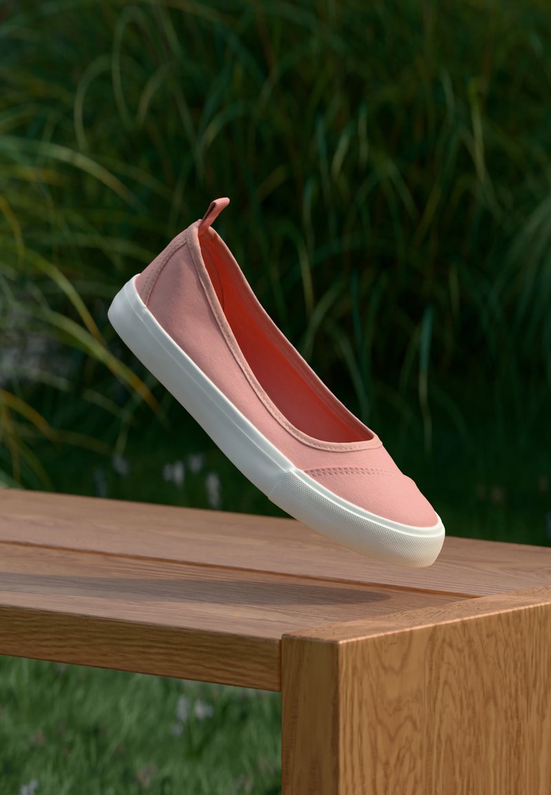 Une chaussure en toile rose unique à enfiler avec une semelle en caoutchouc blanche flottant au-dessus d'un banc en bois en plein air avec des plantes vertes en arrière-plan.