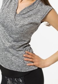 Top atlético gris con escote en V y mangas cortas, hecho de un tejido texturizado que absorbe la humedad, combinado con leggings negros.