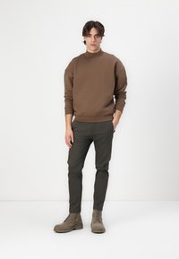 Brown sweatshirt with a high neckline, paired with dark green slim-fit pants and light gray ankle boots with laces. Minimalist design.