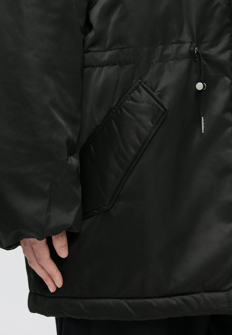 Schwarze Daunenjacke mit glatter, glänzender Oberfläche; verfügt über eine Seitentasche und einen verstellbaren Kordelzug am Saum.