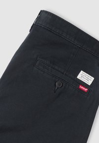 Μαύρο παντελόνι Levi's που εμφανίζει την πίσω τσέπη με κουμπί και τις λευκές και κόκκινες ετικέτες με το λογότυπο Levi's σε ανοιχτό φόντο.
