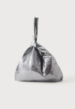 Un sac à main en maille argentée avec une longue bandoulière étroite se trouve sur un fond clair et uni.