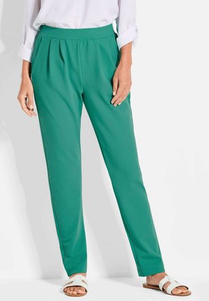 Pantaloni verdi plissettati realizzati in un tessuto liscio con una vita alta, abbinati a sandali bianchi. Il design presenta una silhouette a gamba affusolata.