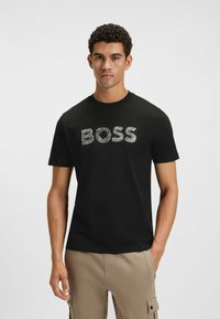 Mustat puuvillateepaidat, joissa on lyhyet hihat ja joka esittelee tekstuurillisen "BOSS"-logon vaaleanharmaana. Pyöreä pääntie muotoilu, jossa on sileä kangaspinta.