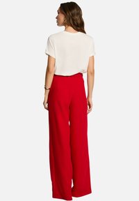 Pantalons larges rouges à taille haute, en tissu lisse. Associés à un t-shirt à col rond blanc. Les détails visibles au dos incluent une ceinture.