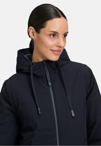 Veste à capuche navy avec fermeture éclair et cordons, présentant une texture lisse et un design épuré.