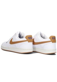 Zapatillas blancas con detalles en marrón, con un upper de cuero texturizado, punta redonda, suela de goma y costuras visibles. "NIKE" en el talón.