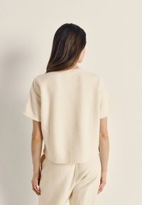 Roomkleurige, gestructureerde top met korte mouwen en een losse pasvorm. Gemaakt van een zacht, pluizig materiaal, met een ronde halslijn en een detail aan de achterkant.