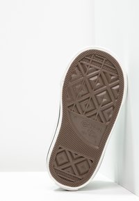 Den brune gummisålen på en Converse All Star-sko har et diamantmønster og merkevarenavnet, med en hvit kant synlig ovenfor.