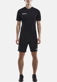 Camiseta atlética negra con cuello en V y mangas cortas, combinada con pantalones cortos a juego. Presenta el logotipo en blanco "CRAFT" en ambos artículos.