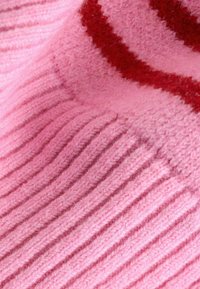 Tissu tricoté rose côtelé avec une texture douce, comportant une bande rouge. Le design inclut des épaisseurs variées dans le motif de tricot.