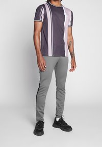 Koszulka z krótkim rękawem w fioletowo-beżowe paski z okrągłym dekoltem, zestawiona z szarymi zwężanymi spodniami z bocznymi paskami oraz czarnymi sportowymi butami.