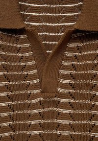Brun strikket polo med hvide striber, der har V-udskæring og et struktureret mønster med hulmønster detaljer. Materiale i bomuldsblanding.