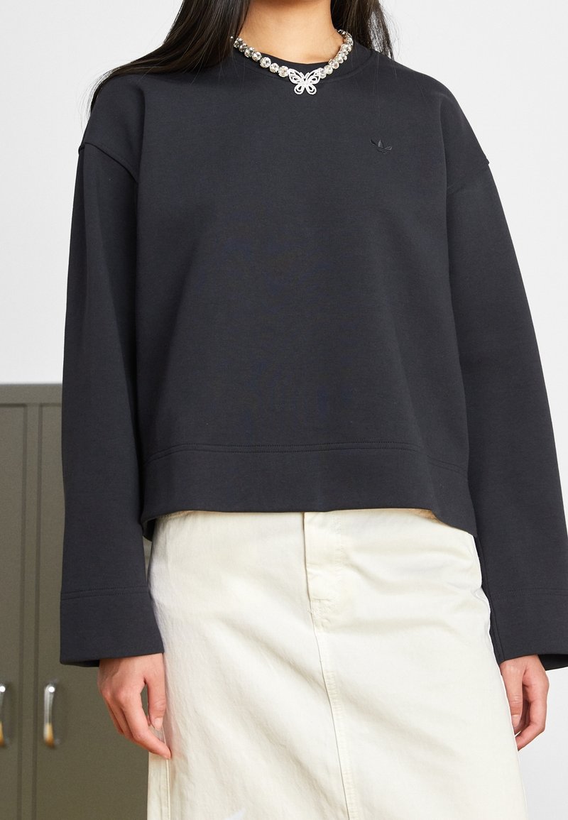 Svart sweatshirt med rund halsringning, långa ärmar och en kortad nederkant. Har en dekorativ pärlkrage och subtil branding på bröstet.