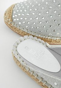 Sidabrinės espadrilės su tekstūruotu paviršiumi, dekoruotu deimantais, pintu jūros žolių viduriu ir baltu guma išoriniu padu su prekės ženklu.