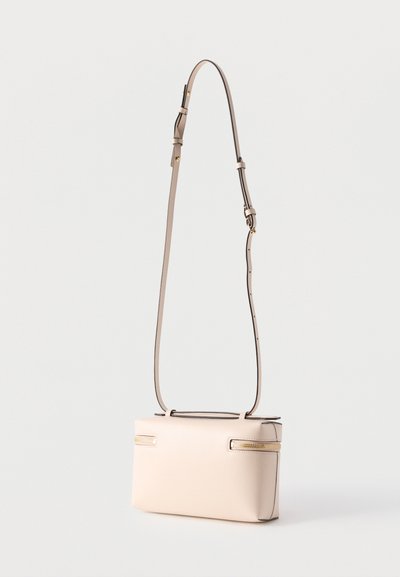 Μπεζ ορθογώνια τσάντα χιαστί με ρυθμιζόμενο ιμάντα και δύο οριζόντιους χρυσούς φερμουάρ στο μπροστινό μέρος, αντικείμενο σε απλό ανοιχτόχρωμο φόντο.