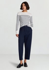 Maglione a righe a maniche lunghe in bianco e blu navy, abbinato a pantaloni navy a vita alta. Tessuto liscio e vestibilità sartoriale. Mocassini neri completano il look.