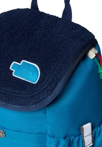 Zils mugursoma ar tumši zilu flīsa pārvalku un gaiši zilu logotipa uzlīmi. Tajā ir teksturēts audums un balti akcenti, kā arī krāsainas rāvējslēdzēja pievilcējas.