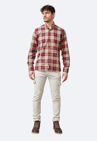 Camisa de manga larga a cuadros en beige, rojo y azul; diseño con botones y cuello, combinada con pantalones cargo de color claro y botas marrones.