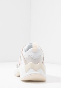 Bílé tenisky s béžovými semišovými detaily, texturovanou síťovinou a výraznou krémovou vlnovitou podrážkou. Mají zadní textilní poutko.