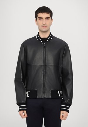 Black leather bomber jacket with a zip front, ribbed collar, and striped cuffs. Features a knit hem with contrasting branding detail.