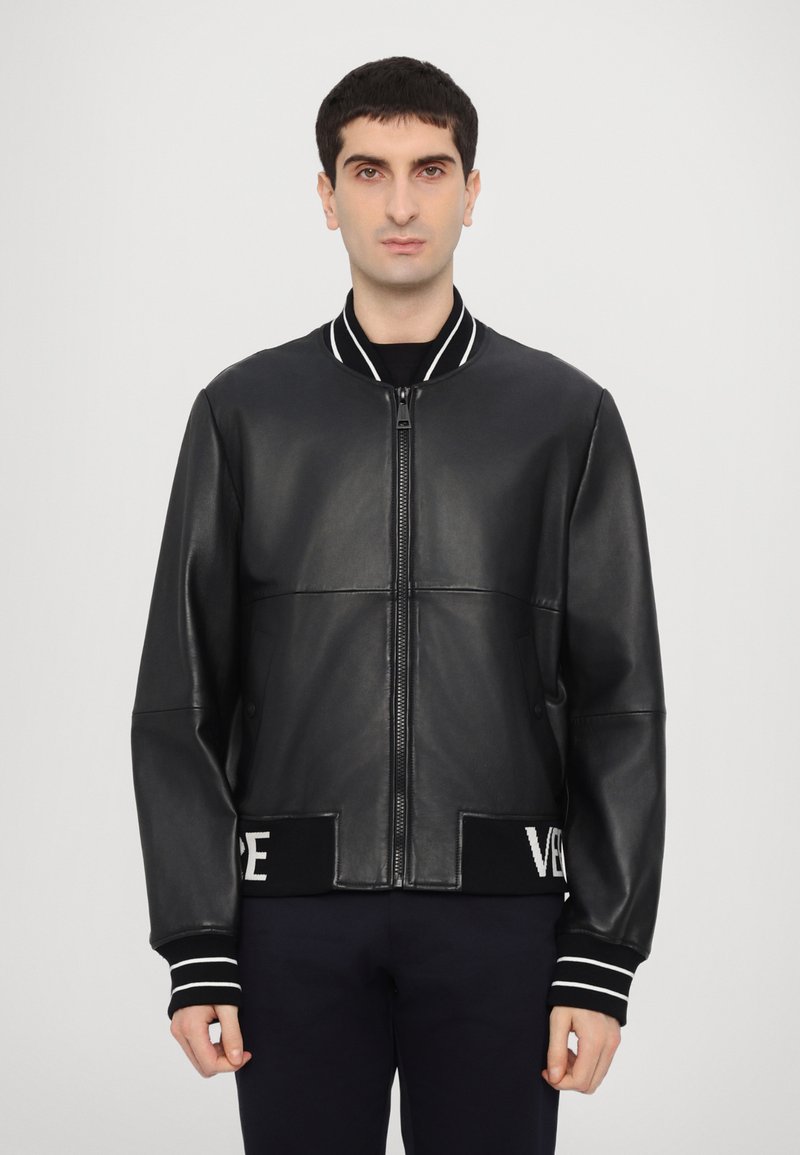 Jachetă bomber din piele neagră, cu fermoar frontal, guler ribbed și manșete cu dungi. Dispune de o margine tricotată cu detalii de brand contrastante.