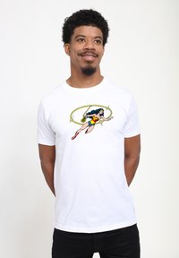 Camiseta blanca de algodón que presenta un gráfico colorido de Wonder Woman, incluyendo su icónico lazo, sobre un fondo liso.
