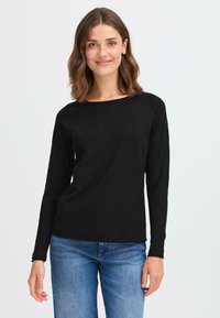 Sort langermet topp i svart laget av et mykt stoff med rund hals. Designet har en tettsittende fasong og glatt tekstur. Brukt med blå jeans.