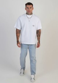 Camiseta blanca de algodón con un corte holgado y mangas cortas, combinada con jeans azul claro. El conjunto presenta elementos de diseño minimalistas.