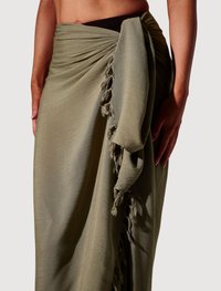 Jupe portefeuille vert olive en tissu léger et fluide. Elle présente un détail noué et un ourlet à franges, avec une surface douce légèrement texturée.