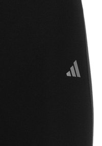 Pantalons de sport noirs fabriqués en tissu texturé, avec un logo réfléchissant avec trois rayures diagonales sur le bas à gauche.